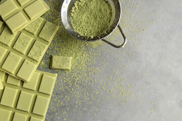 Pieces of tasty matcha chocolate bars and powder on grey textured table, flat lay. Space for text
