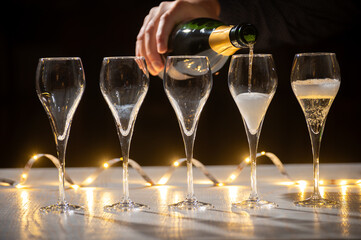 New year party, pouring of brut champagne bubbles cava or prosecco wine in tulip glasses with garland  lights on background