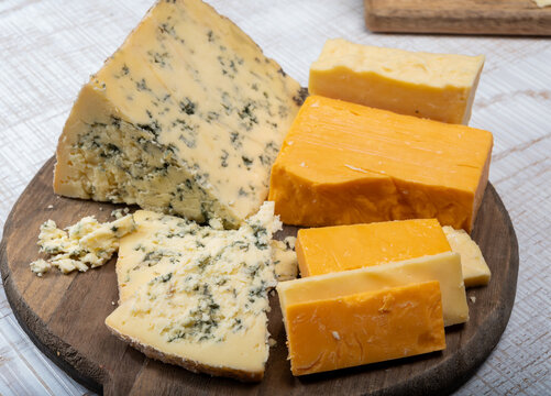 English cheeses collection, mature and coloured cheddar cheese and semi-soft, crumbly old stilton blue cheese close up
