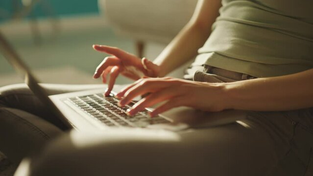 Cropped view of caucasian young woman sitting on the floor beside sofa in living room, working and typing on laptop