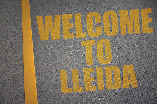 asphalt road with text welcome to Lleida near yellow line.