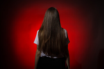 A woman is viewed from behind, looking over her shoulder against a red background, giving a sense...