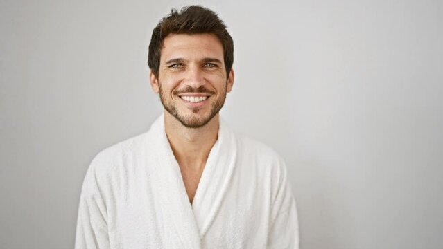 A handsome young hispanic man with a beard smiles in a white robe against an isolated white background