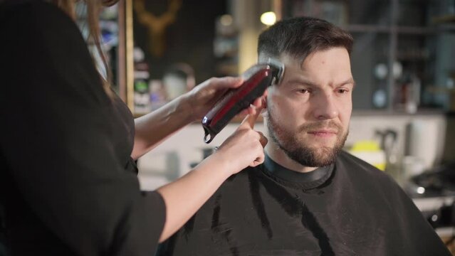 Young female barber making men's undercut haircut hairstyle using Haircut Clipper in Modern style barber shop. Haircare service local small business, cosmetics and personal care industry 4K video