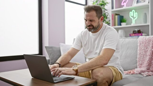 Mature man with grey hair using laptop at home, depicting remote work in a comfortable living room setting.