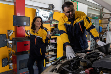 Professional Uniformed Car Mechanic Working in Service Station. Team Discussing and Repairing Vehicle. Car's Engine in The Uniform Works in The Automobile Selective Focus