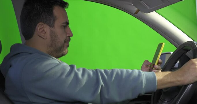 a man texting with his smart phone inside his car, on green screen, driving concept