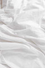 White fabric texture background, wavy cloth. Crease bedclothes fragment as background, Crumpled sheet of bed. White bed linen as minimal backdrop. Top view aesthetic surface, screensaver