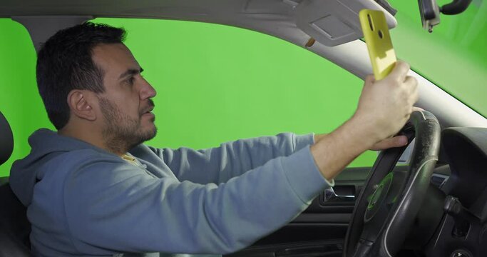 a man taking a selfie with his smart phone inside his car with a green background
