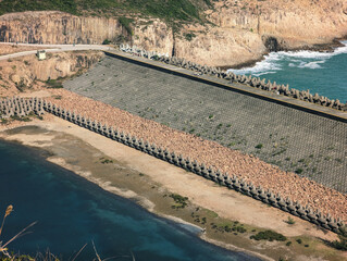 Fototapeta premium A large dam with tetrapod wave breakers, surrounded by a rocky landscape and the sea. 