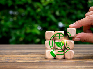 Earth care, global warming, environment responsibility, world earth day concepts. Green hand hold world, symbol in hand put on wooden cube puzzle blocks on green leaves background with copy space.