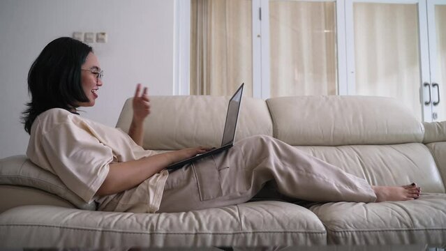 beautiful asian young woman wear casual sit on couch using computer laptop relax smile and laughing
