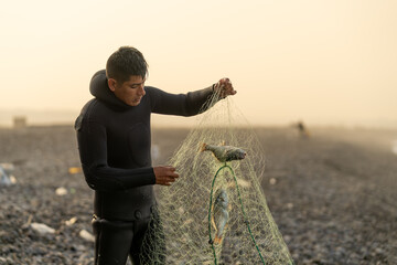 Latin fisherman in wetsuit removing trapped fish from a net