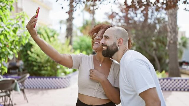 Beautiful couple smiling, standing together in park, enjoying outdoor selfie fun with smartphone