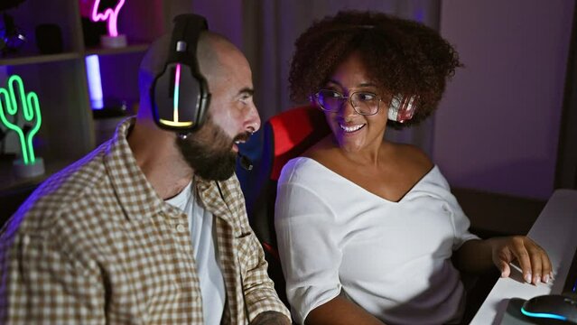 Two gamers smiling confident sitting on table speaking at gaming room