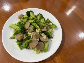A plate of stir fry broccoli with garlic and sliced meatballs on wood table background