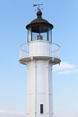 White lighthouse tower with black roof and vane is under blue sky on a daytime