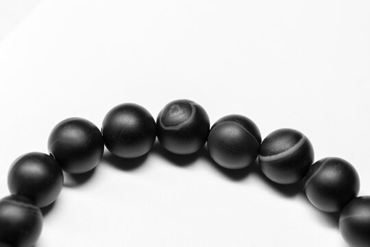 Bracelet made of round black agate beads lays on white background, close-up
