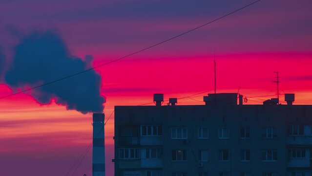 Beautiful red dawn on background of a high-rise apartment building and chimney of a thermal power plant. Time lapse ethical red-pink dawn in city. Close-up. Smoke is coming out of the TPP chimney