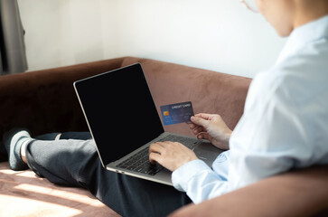 Asian girl shopping online holding credit and using laptop enter their card number in the mobile phone app to purchase and payment in internet store