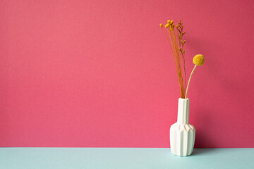 Vase of yellow dry flowers on skyblue table. pink wall background