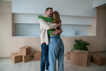 Man hugging woman in new apartment just moving in it together as family couple. Wife husband cuddling enjoying life changings. Loving spouses standing among cardboard boxes relocating in new flat. 