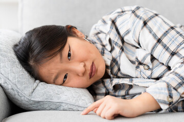 Depressed asian woman looking at camera with sad expression lying on the sofa