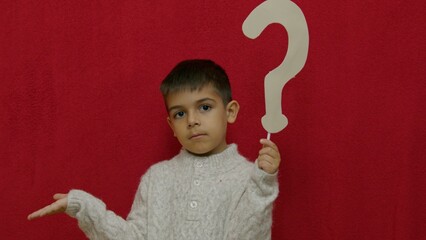 Cute child questioning something. Holding question mark , isolated on red with copy space. High...