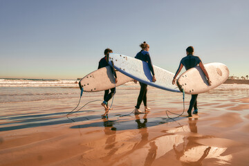 Group of surfers with surfboards in wetsuit are walking on the beach after ride the waves