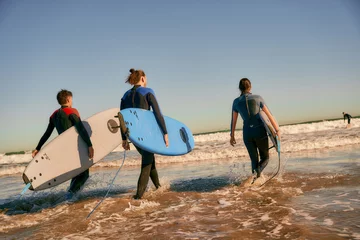 Fotobehang Group of friends with surfboards entering towards ocean for surfing on waves. High quality photo © Daria