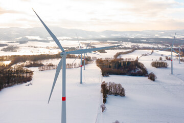 Amidst a frozen landscape with wind turbines, standing in the winter field at sunset. 