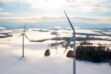Windmills in a wintery expanse at sundown and mountains on the background. Wind turbines for green...