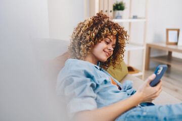 Smiling Woman Holding Mobile Phone, Enjoying Online Game and Chatting in Cozy Living Room