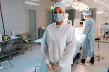 Portrait of pretty African-American female doctor standing posing looking at camera in operating...