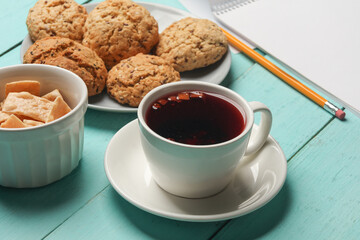 Cup of tea with cookies and sketchbook on blue table
