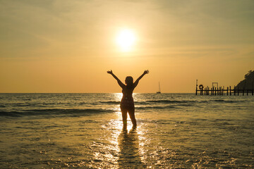 Asian women in bikini swimsuit silhouette with raised arms against calm sunset beach. Happy woman...