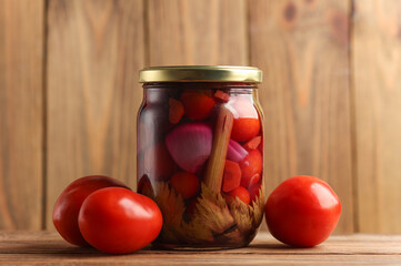 Pickled Canned tomatoes in glass jar on wooden surface
