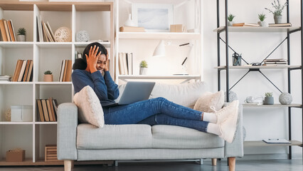 Internet conflict. Video conversation. Emotional expressive stressed woman quarreling at laptop online meeting on couch in living room at home.