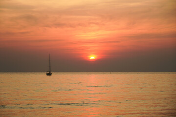 Sunset on the beach with long coastline, sun and dramatic sky. Tropical sea sunset. Sky background. Bright beautiful sunrise or sunset at sea.