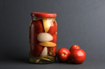 Pickled Canned tomatoes in glass jar on dark gray background
