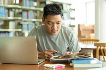 Fotobehang male asian student studying and reading book in library © Pormezz