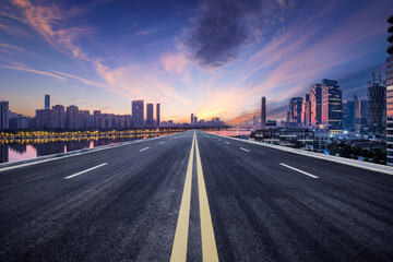 Empty asphalt and city buildings skyline at sunset