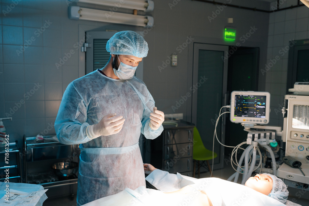 Poster Portrait of professional male surgeon in protective workwear standing by operating table with female patient lying down before next difficult operation. Concept of surgery and emergency.