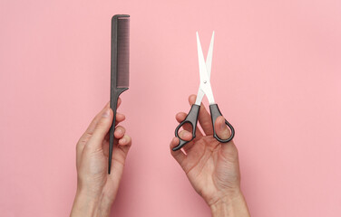 Female hands holding haircutting scissors and comb on a pink background