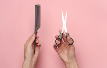  Female hands holding haircutting scissors and comb on a pink background © splitov27