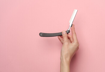 Hand holding a straight razor on a pink background - obrazy, fototapety, plakaty