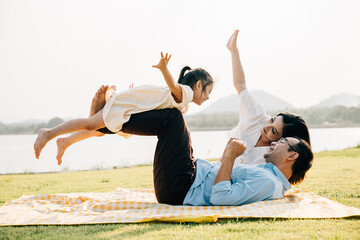 A family enjoys playful moments together. Father holds daughter high in air as she giggles and...