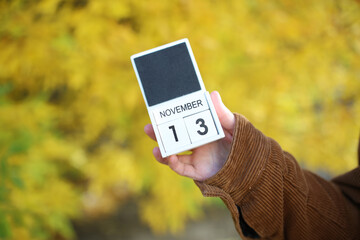 Woman holding calendar with date november 13 on yellow autumn leaves background