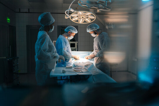 Remote portrait of diverse cooperating team of doctors, surgeons and African-American nurse processing surgical operation in operating room modern hospital emergency department. Concept of surgery.
