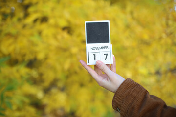 Woman holding calendar with date november 17 on yellow autumn leaves background